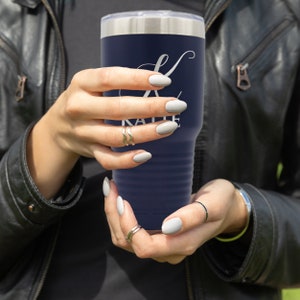 May include: A navy blue stainless steel tumbler with a white initial "K" and the name "Katie" printed on the side. The tumbler is being held by a person's hands.