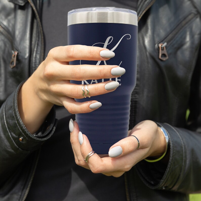 May include: A navy blue stainless steel tumbler with a white initial "K" and the name "Katie" printed on the side. The tumbler is being held by a person's hands.