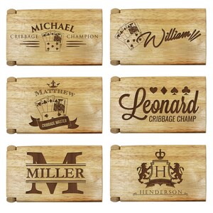 Puede incluir: Seis cajas de madera con diferentes grabados personalizados. Las cajas presentan nombres como "Michael", "William", "Matthew", "Leonard", "Miller" y "Henderson". Algunas cajas incluyen im&aacute;genes de cartas de juego y t&iacute;tulos como "Campe&oacute;n de Cribbage" y "Maestro de Cribbage".