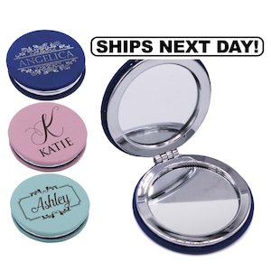 May include: A collection of round compact mirrors with silver-toned metal frames. Three closed mirrors are shown in blue, pink, and light blue, each featuring personalized names and decorative flourishes. One open blue mirror reveals two reflective surfaces.