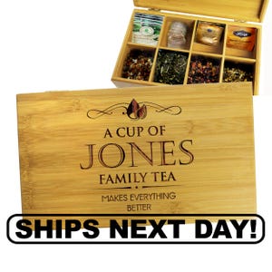 May include: A bamboo tea box with a hinged lid, featuring compartments filled with various tea bags and loose-leaf teas. The lid is engraved with the text "A CUP OF JONES FAMILY TEA MAKES EVERYTHING BETTER".