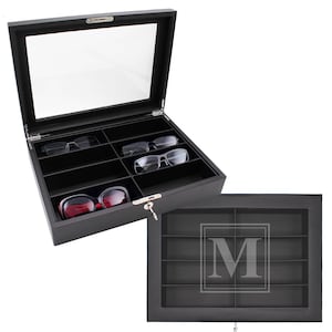 May include: Black eyeglass display case with a clear glass top and multiple compartments. The case is open, revealing several pairs of eyeglasses. A second, closed case with an etched "M" is also shown.