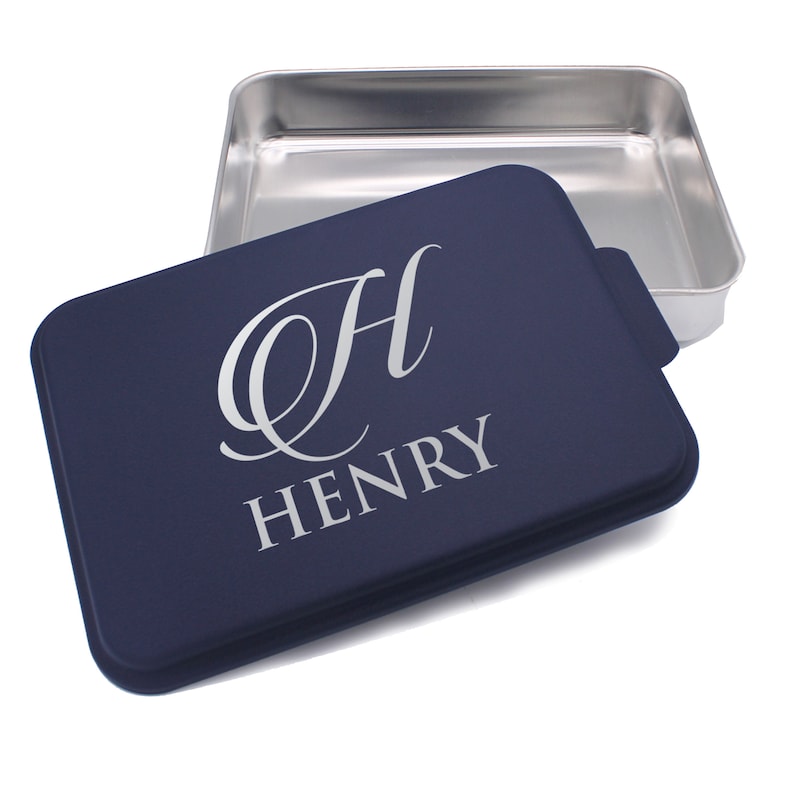 May include: A navy blue cake pan with a silver lid. The lid has the letter "H" and the name "HENRY" engraved on it.