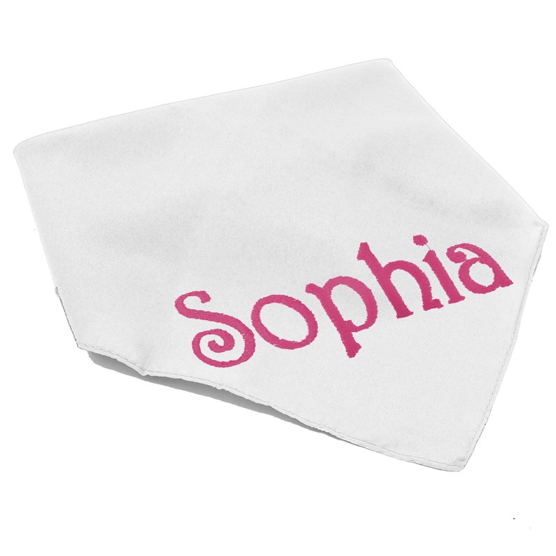 May include: A white triangular bandana featuring the name Sophia printed in a bold, dark pink font across the center. The fabric has a smooth texture and clean, finished edges, presenting a simple design with the name clearly visible in pink.