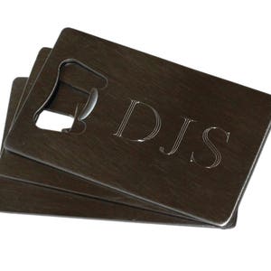 May include: A set of three stacked metal bottle openers with a cutout design and the initials "DJS" engraved on the top opener.
