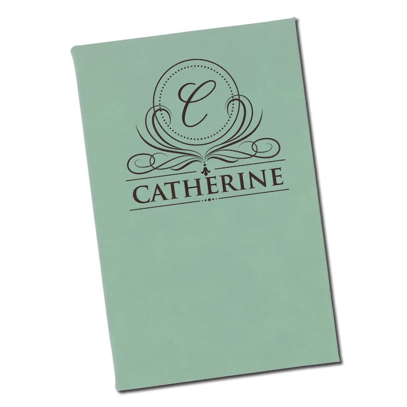 Puede incluir: Un cuaderno verde claro personalizado con el nombre "Catherine" impreso en marr&oacute;n oscuro. El dise&ntilde;o incluye un monograma circular con la letra "C" y adornos decorativos.
