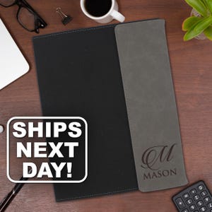 May include: A black portfolio folder featuring a vertical gray panel on the right side. The gray panel is engraved with a large cursive letter M above the name MASON in capital letters. A white rectangular graphic displays the text SHIPS NEXT DAY!