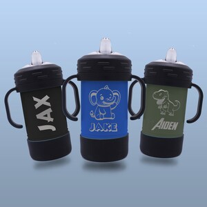 May include: Three personalised sippy cups with different animal designs and names. The cups are black with blue, green, and black accents. The names on the cups are Jax, Jake, and Aiden.