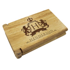 Puede incluir: Una caja de madera con tapa con bisagras, grabada con un escudo que presenta una corona, un escudo con la letra "H" y dos leones. La caja est&aacute; personalizada con el nombre "Henderson".
