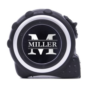 May include: Black and silver tape measure with the name "MILLER" in white. The tape measure is black with a silver rim and a black center. The tape measure is a construction tool.