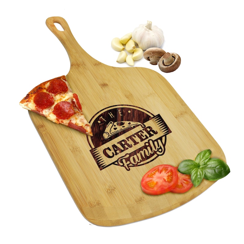 May include: A wooden pizza serving board with a handle, featuring a slice of pepperoni pizza, sliced tomatoes, basil, garlic, and mushrooms. The board is engraved with "The Carter Family" and a pizza graphic.