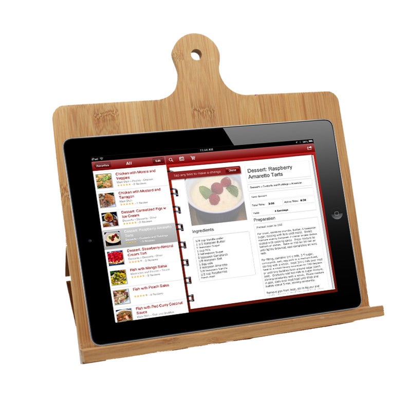 Może przedstawiać: Jasnobrązowy bambusowy stojak na tablet w kształcie deski do krojenia z uchwytem i otworem u g&oacute;ry. Na stojaku spoczywa czarny tablet, na kt&oacute;rym wyświetlany jest cyfrowy przepis na tartaletki z amaretto i malinami wraz z listą składnik&oacute;w.