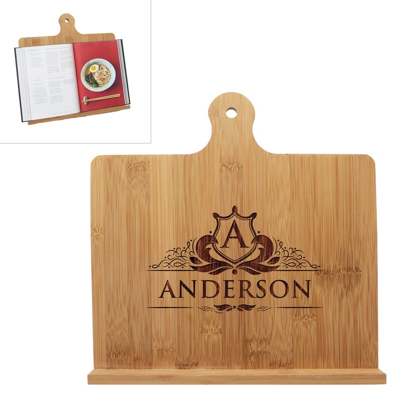 May include: A light brown bamboo cookbook stand featuring a handle with a circular cutout at the top and a horizontal ledge at the base. The center is laser-engraved with a decorative crest containing the letter A and the name ANDERSON below.