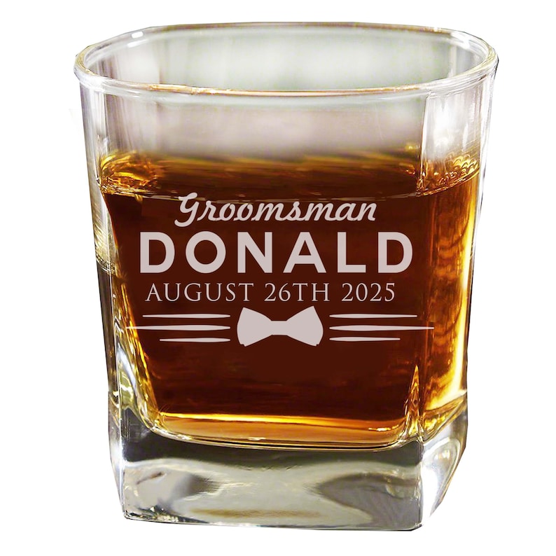 May include: A clear glass rocks glass with a personalized inscription that reads "Groomsman DONALD AUGUST 26TH 2025" with a bow tie graphic.