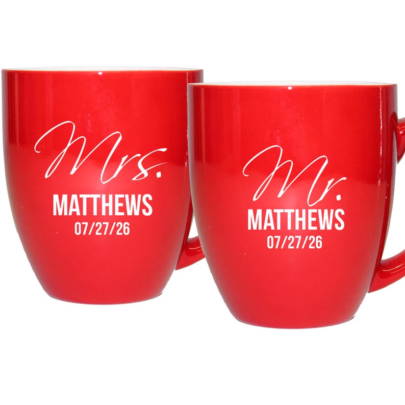 May include: Two red ceramic mugs with white text. One mug reads "Mrs. MATTHEWS 07/27/26" and the other reads "Mr. MATTHEWS 07/27/26". Both mugs have a curved shape and a handle.