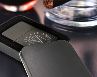 May include: A silver lighter in a black case with the name "Vincent" engraved on it. The lighter is surrounded by a laurel wreath.