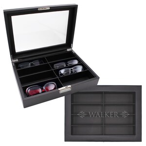 May include: A black rectangular eyewear storage case with a clear glass lid and a silver metal latch. The interior features eight individual compartments lined in black fabric. The lid is engraved with the name WALKER and decorative flourishes.