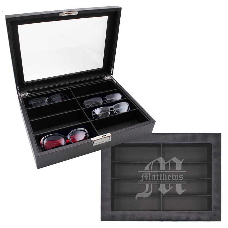 May include: A black textured storage box for eyewear with a glass lid and a metal latch. The interior features eight compartments, with three pairs of glasses inside. The lid is engraved with a large letter M and the name Matthews in white text.