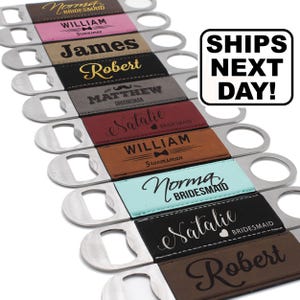 May include: A collection of metal bottle openers with rectangular, colored, and textured grips. Each grip is personalized with names and titles like Bridesmaid or Groomsman in various fonts. A white sign with black text reads SHIPS NEXT DAY.