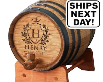 May include: A wooden barrel with black metal hoops, resting on a light wood stand. The front features a laser-engraved crest with the letter H, the name HENRY, and the text EST 2021. A wooden spigot is attached to the front. Text reads SHIPS NEXT DAY!