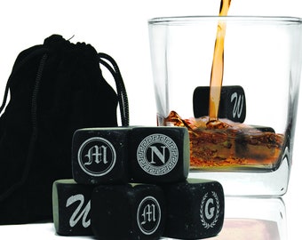 May include: Set of six black engraved whiskey stones in a black velvet bag. The stones are engraved with the letters M, N, W, M, G, and U. The stones are in a glass with whiskey being poured into it.