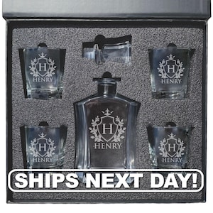 May include: A clear glass decanter and four matching glasses set inside a black foam-lined box. Each piece features an etched crest design with the letter H and the name HENRY. A glass stopper is included in the top center of the foam insert.