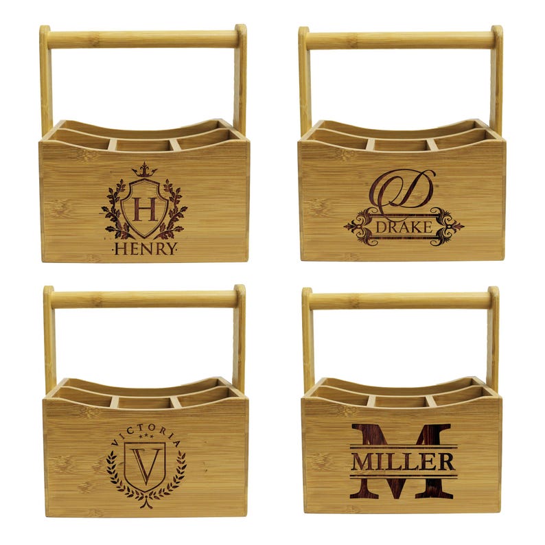 Może przedstawiać: Cztery drewniane przenośne pojemniki na butelki z uchwytami. Każdy pojemnik ma inny grawerowany wz&oacute;r z nazwą i inicjałem. Wzory obejmują herb z literą H dla Henry'ego, monogram z literą D dla Drake'a, herb z literą V dla Victorii i duże M dla Millera.