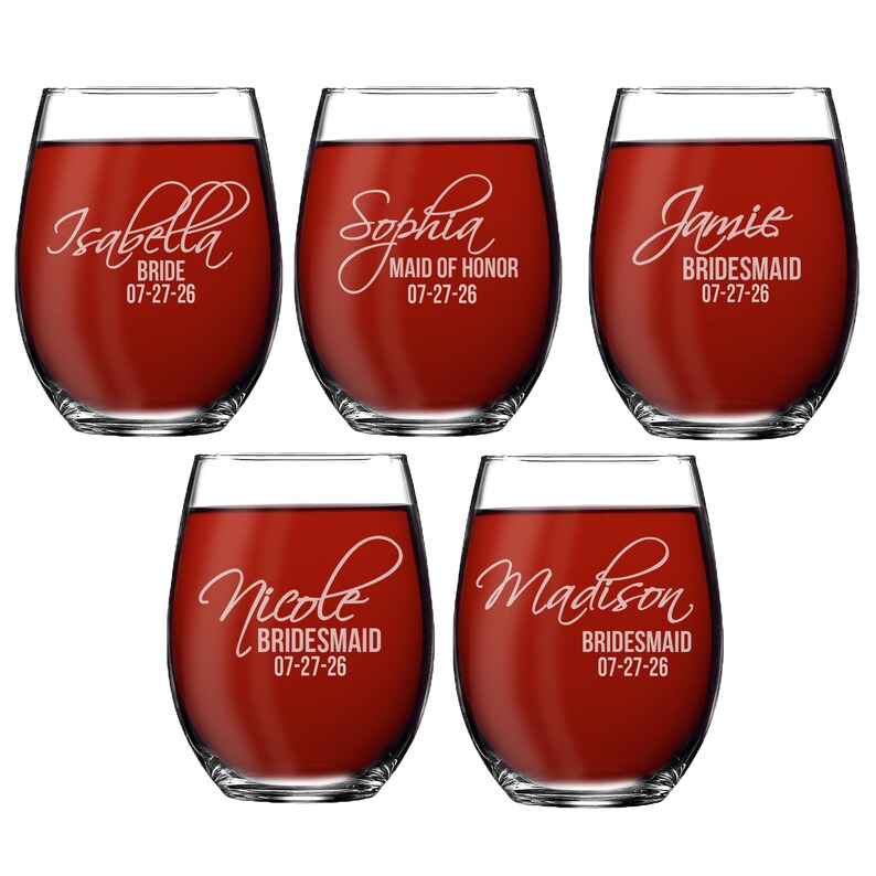 May include: Five stemless wine glasses filled with red liquid. Each glass has a name and role, such as "Isabella Bride" and "Sophia Maid of Honour", with the date "07-27-26" below. The glasses are clear with white lettering.