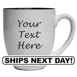 May include: White ceramic mug with a black rim and handle. The mug features the text "Your Text Here" in a black, cursive font. The mug is designed for customization. The bottom of the mug has a black and white banner that says "SHIPS NEXT DAY!"