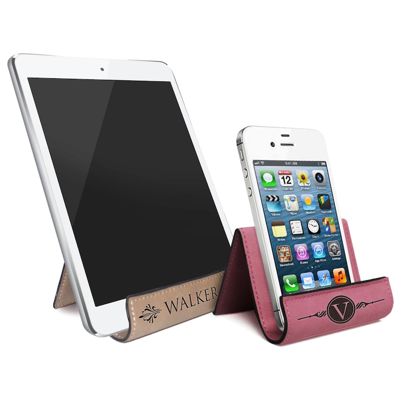 May include: Two phone stands, one in pink and one in brown, with a personalized inscription. The pink stand has a white phone in it, and the brown stand has a white tablet in it. The inscription on the brown stand reads "WALKER".