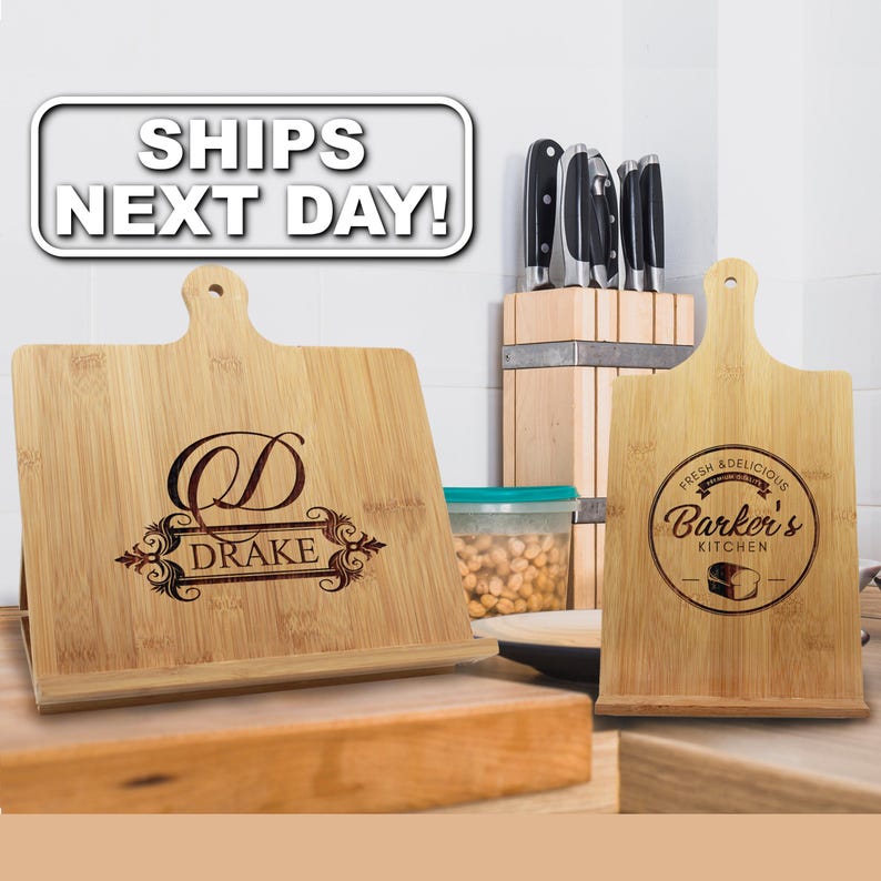 May include: Two light-colored bamboo wood recipe stands with laser-engraved designs. The left stand features a large letter D and the name DRAKE. The right stand displays a circular logo with the text FRESH & DELICIOUS BARKER'S KITCHEN.