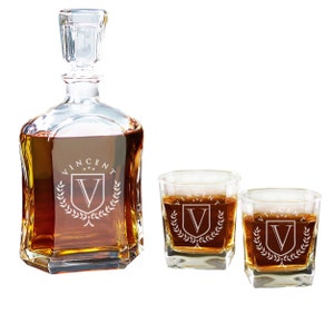 May include: A clear glass decanter with a matching stopper and two square whiskey glasses, all filled with amber liquid. Each piece features an etched design of a shield with the letter V, the name VINCENT, and three stars above it.