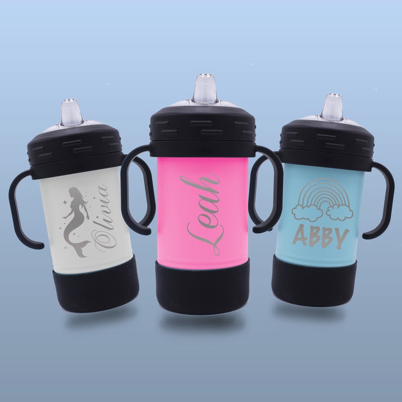 May include: Three personalised stainless steel sippy cups with different designs. The first cup is white with a mermaid design and the name "Olivia" engraved on it. The second cup is pink with the name "Leah" engraved on it. The third cup is blue with a rainbow and clouds design and the name "Abby" engraved on it.