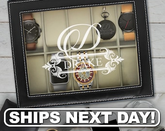 May include: A black rectangular watch display case with a glass lid featuring a white monogram letter D and the name DRAKE printed in the center. The interior contains multiple beige velvet compartments holding various wristwatches and a pocket watch.