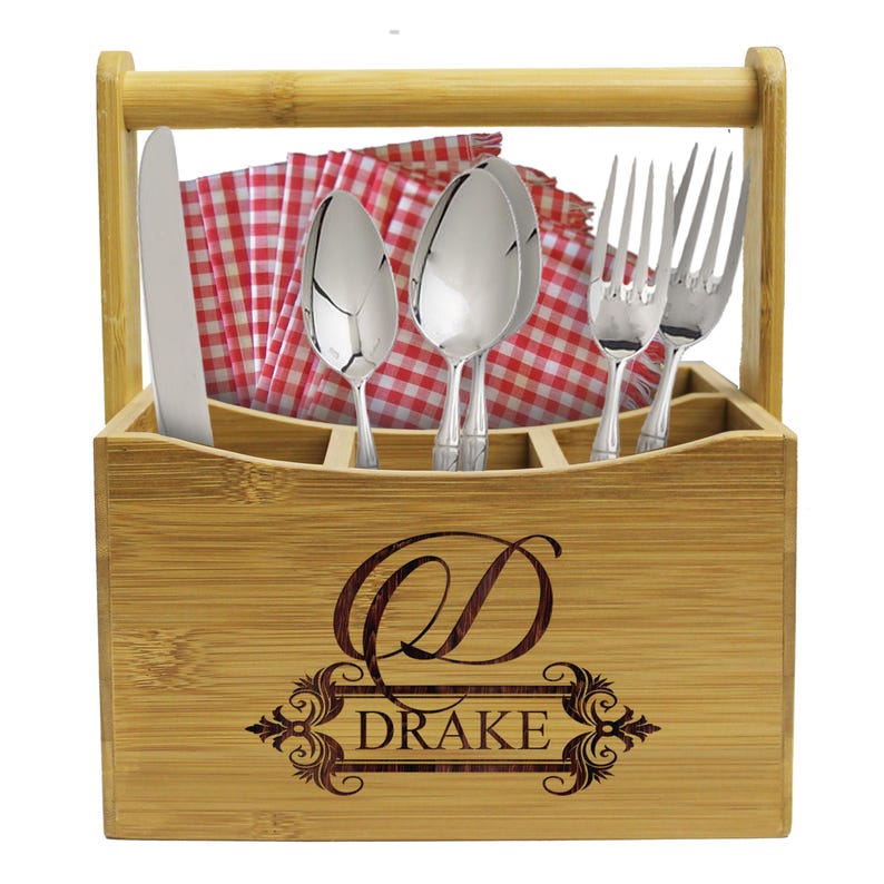 Może przedstawiać: Bambusowy pojemnik na sztućce z uchwytem, sześcioma przegr&oacute;dkami na sztućce i czerwoną w białą kratkę serwetką. Pojemnik jest grawerowany literą "D" i nazwiskiem "DRAKE".