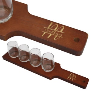 K&ouml;nnte beinhalten: Ein Bier-Flight-Set aus Holz mit vier kleinen Gl&auml;sern und einem gr&ouml;&szlig;eren Glas. Das Set besteht aus dunkelbraunem Holz und tr&auml;gt den Namen "Matthews" in goldfarbener Schrift. Die Gl&auml;ser sind klar und leer.