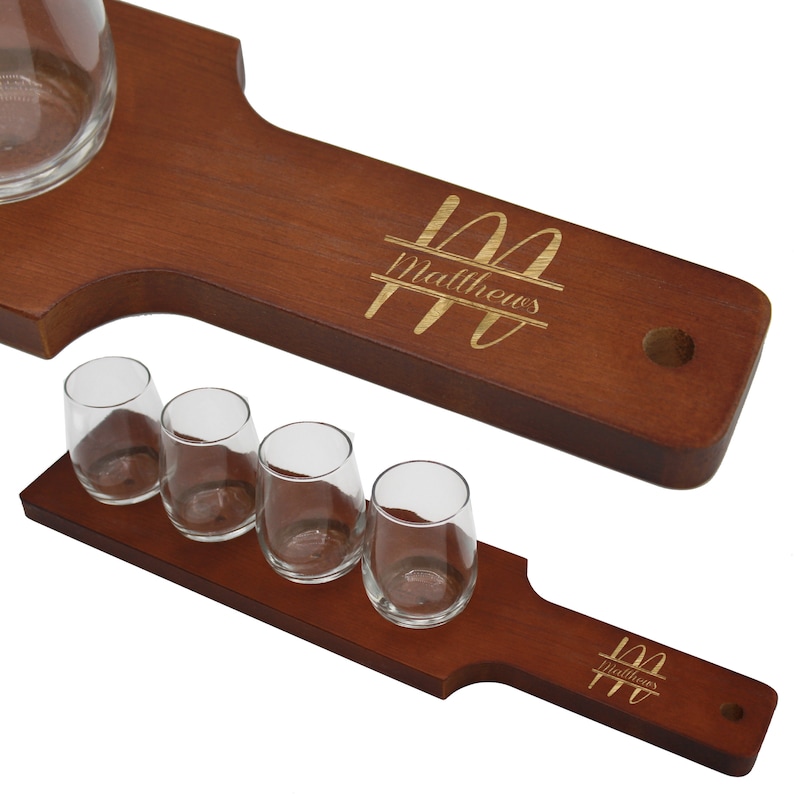 K&ouml;nnte beinhalten: Ein Bier-Flight-Set aus Holz mit vier kleinen Gl&auml;sern und einem gr&ouml;&szlig;eren Glas. Das Set besteht aus dunkelbraunem Holz und tr&auml;gt den Namen "Matthews" in goldfarbener Schrift. Die Gl&auml;ser sind klar und leer.