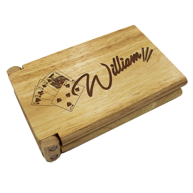 Puede incluir: Una caja de madera con tapa abatible, personalizada con el nombre "William" y una imagen de cartas de juego. La caja est&aacute; hecha de madera marr&oacute;n claro y tiene un acabado natural.