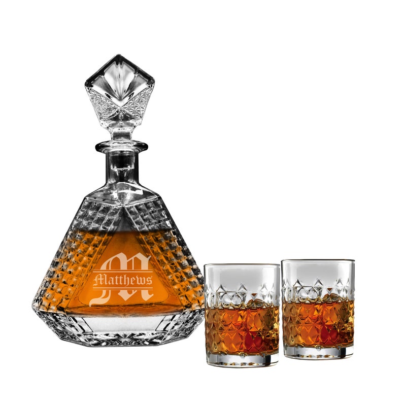 May include: A clear glass decanter with a diamond-cut pattern and a matching stopper, featuring the engraved name Matthews over a large letter M. Two matching clear glass tumblers with a diamond-cut base are filled with an amber-colored liquid.