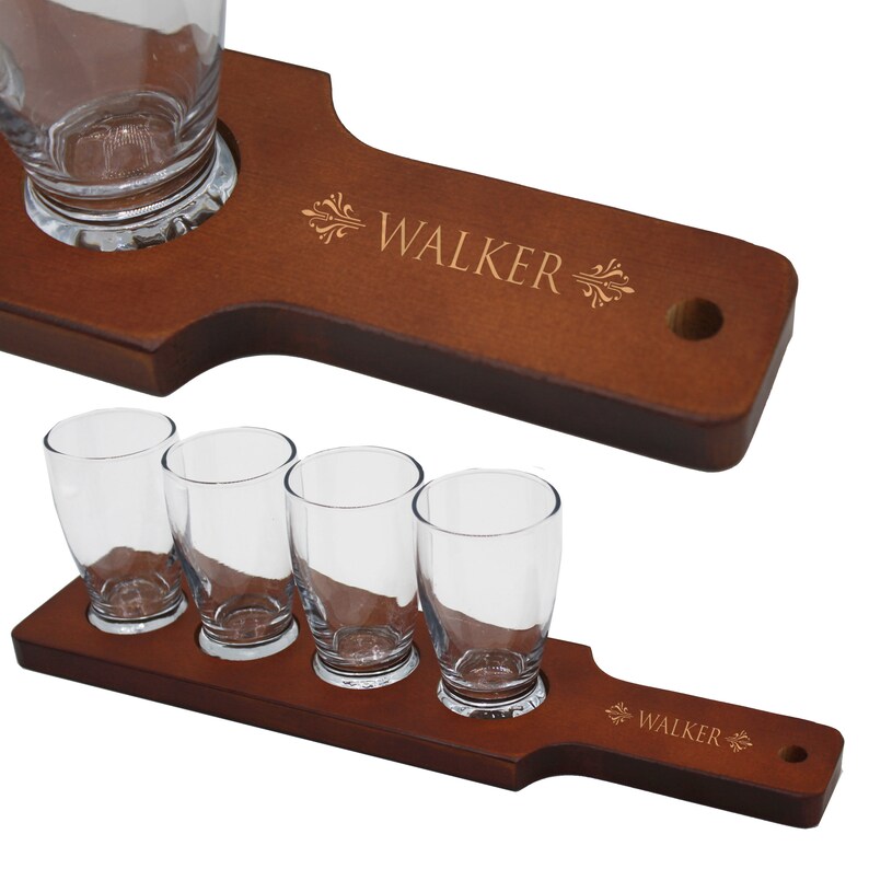 May include: Two wooden beer flight boards with clear glasses. One board holds four glasses, the other holds one. The boards are engraved with the name "WALKER" and decorative flourishes. The wood has a warm, brown finish.