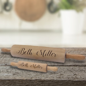 Puede incluir: Dos rodillos de madera, uno grande y otro peque&ntilde;o, con mangos de madera. El nombre "Beth Miller" est&aacute; grabado en cursiva en cada rodillo. Los rodillos se muestran sobre una superficie de madera r&uacute;stica.