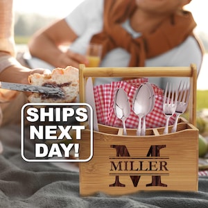 May include: A rectangular bamboo utensil caddy with a handle, featuring the engraved letter M and the name MILLER on the front. The caddy holds silver-toned spoons, forks, and a knife, along with red and white checkered napkins. Text reads SHIPS NEXT DAY!
