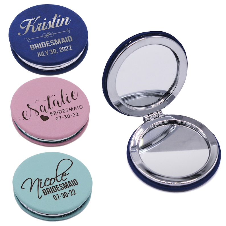 May include: Three round compact mirrors in blue, pink, and light blue with silver metallic edges. Each mirror features custom text including names like Kristin, Natalie, and Nicole, the title BRIDESMAID, and the date 07-30-22. One mirror is open.