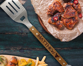 May include: A stainless steel barbecue spatula with a wooden handle engraved with the name "MATTHEW". The spatula has a bottle opener and slots for draining. The image also shows grilled chicken wings, corn, and fries.
