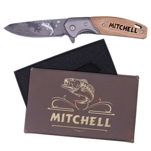以下が含まれることがあります： 木製のハンドルと「MITCHELL」の名前が刻まれたパーソナライズされた折りたたみナイフ。 刃には魚のグラフィックがあります。 ナイフは、「MITCHELL」と魚のグラフィックが刻まれた茶色の箱と一緒に表示されます。