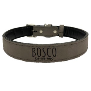 Op de afbeelding: Een grijze hondenriem met de naam "BOSCO" en een telefoonnummer in zwarte letters. De halsband heeft een zilveren gesp en klinknagels. De binnenkant van de halsband is zwart.