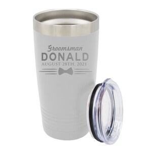 May include: A gray stainless steel tumbler with a black lid. The tumbler has the text "Groomsman DONALD AUGUST 28TH, 2021" and a bow tie graphic.