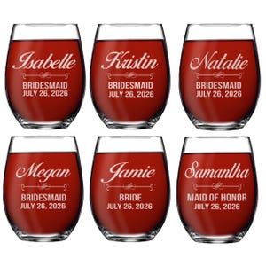 May include: Six clear stemless wine glasses filled with red liquid. Each glass is etched with a name, a title, and the date JULY 26, 2026. The names are Isabelle, Kristin, Natalie, Megan, Jamie, and Samantha. Titles include BRIDESMAID, BRIDE, and MAID OF HONOR.