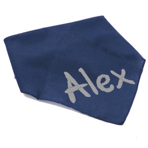 May include: A triangular navy blue fabric bandana featuring the name Alex embroidered in light gray thread across the lower right corner. The accessory has a smooth texture and clean stitched edges, presenting a simple and functional design.