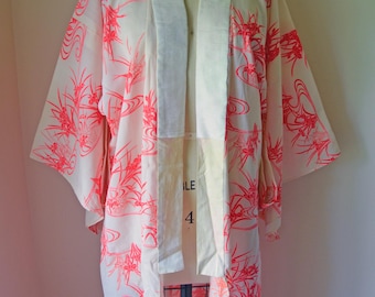 May include: A white kimono-style robe with a vibrant coral floral pattern. The robe features wide sleeves and a contrasting white collar and trim. The garment is displayed on a mannequin, showcasing its flowing design and intricate details.